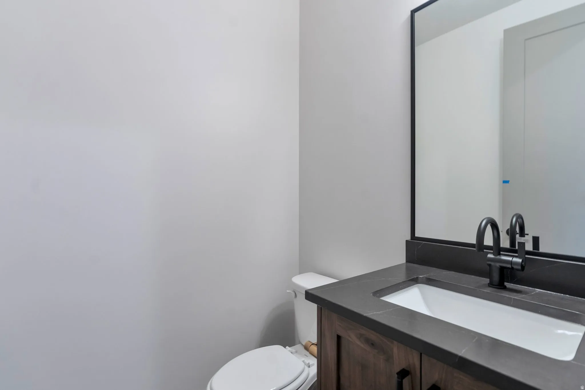 Bathroom vanity featuring a dark wood-finish cabinet with black hardware, a dark countertop with an integrated white rectangular sink, and a matte black faucet