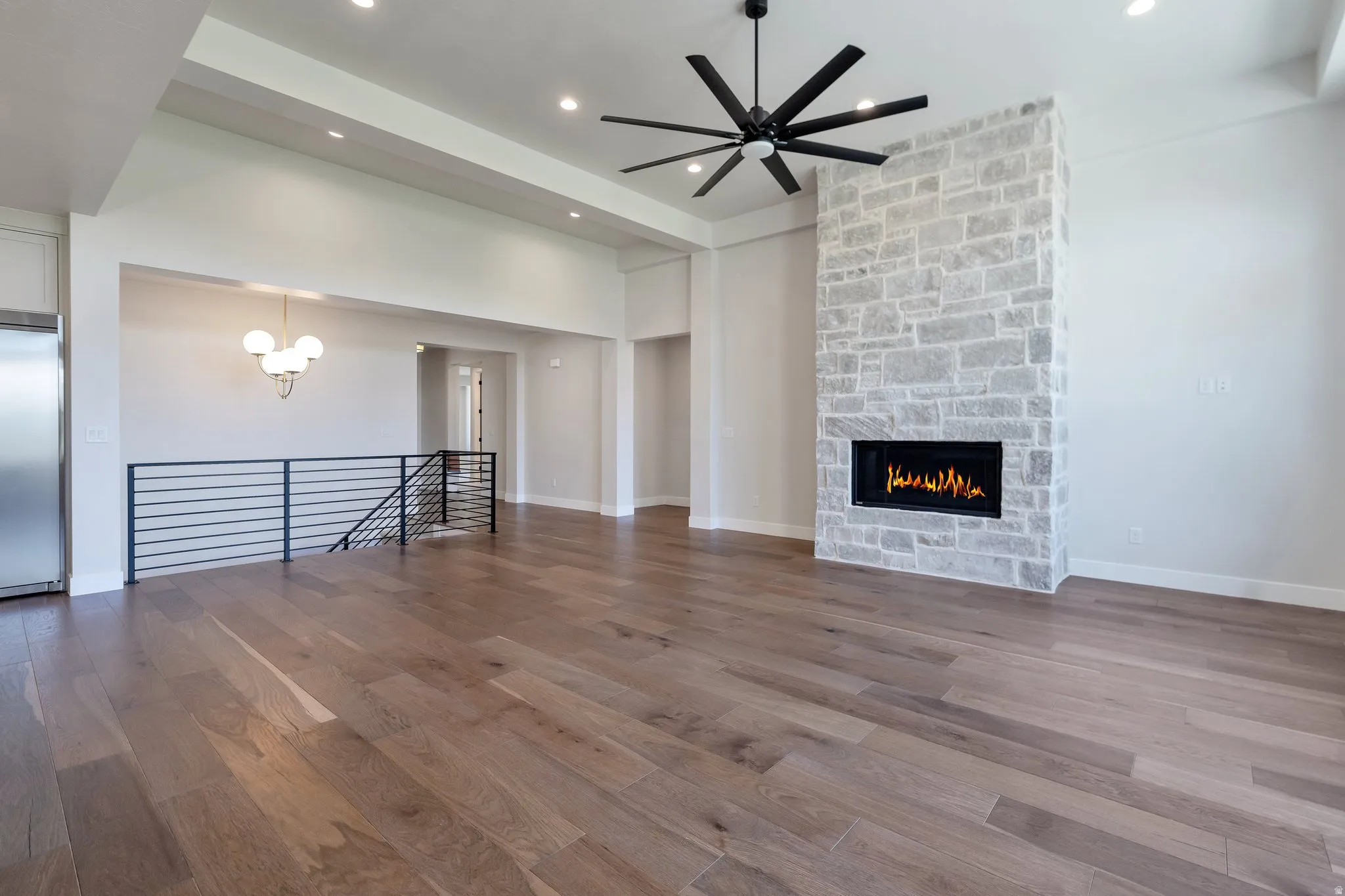 Spacious living area featuring wood-finish flooring, a contemporary stone fireplace, and a large ceiling fan
