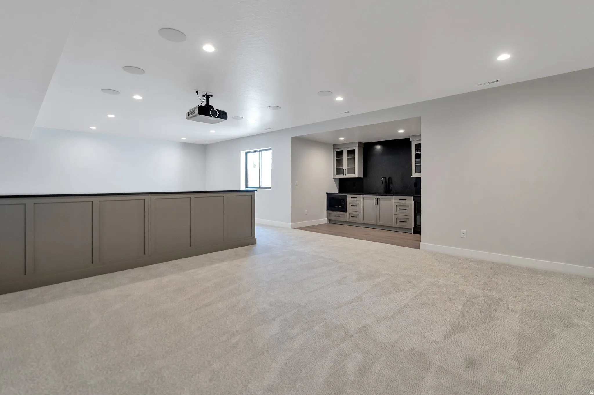 Spacious open room featuring light-toned carpeting, recessed ceiling lighting, and a built-in projector system