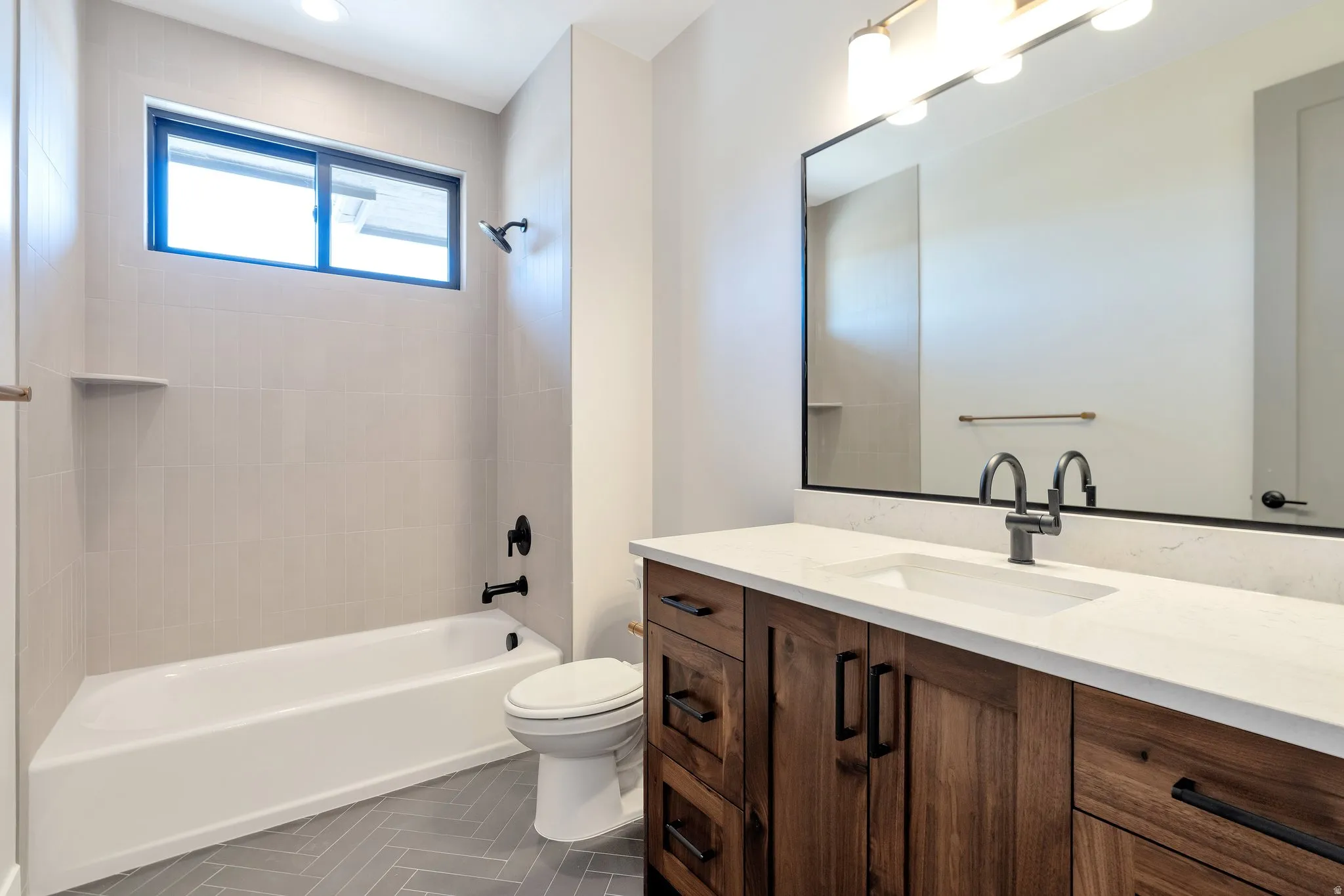 Bathroom featuring a wood-finish vanity with white countertop, integrated sink, and matte black hardware