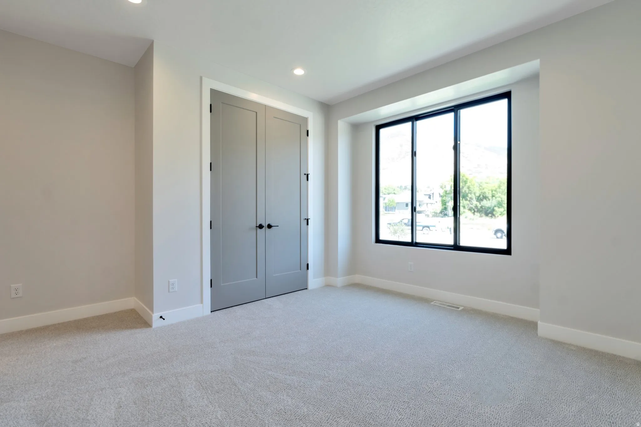 Light-filled room featuring recessed lighting, neutral wall tones, plush gray carpeting, and a three-panel window with black framing