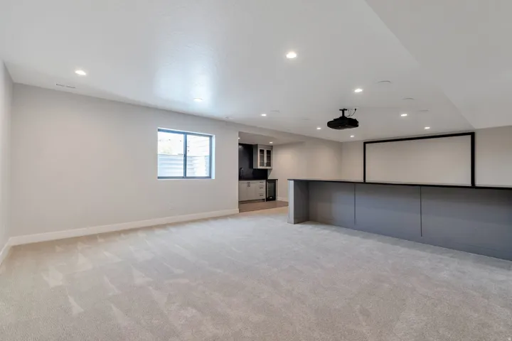 Spacious entertainment area featuring a built-in media screen, overhead projector, recessed lighting, and a wet bar with shaker cabinetry