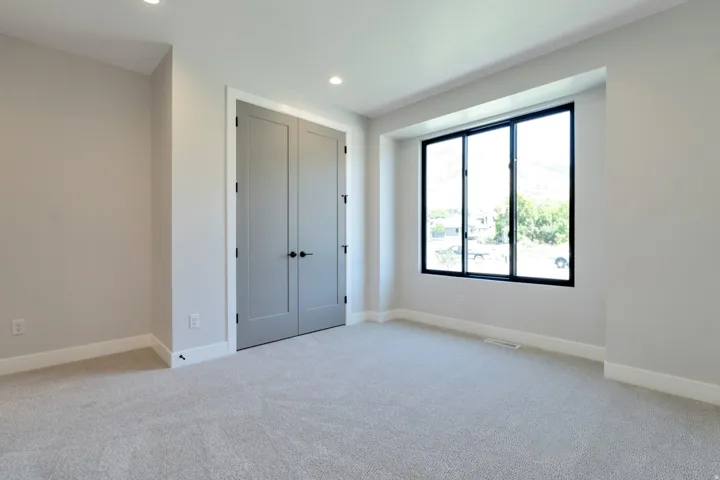 Light-filled room featuring recessed lighting, neutral wall tones, plush gray carpeting, and a three-panel window with black framing