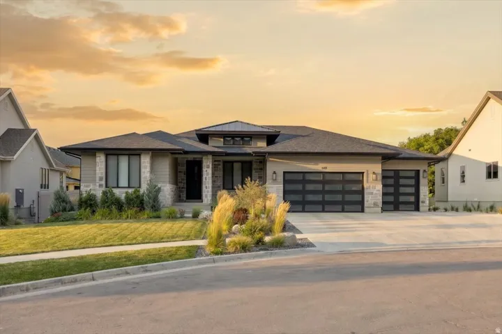Modern residence featuring a stone and stucco exterior, prominent dark-framed windows, and a multi-car garage with contemporary glass panel doors
