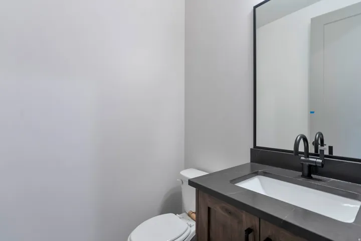 Bathroom vanity featuring a dark wood-finish cabinet with black hardware, a dark countertop with an integrated white rectangular sink, and a matte black faucet