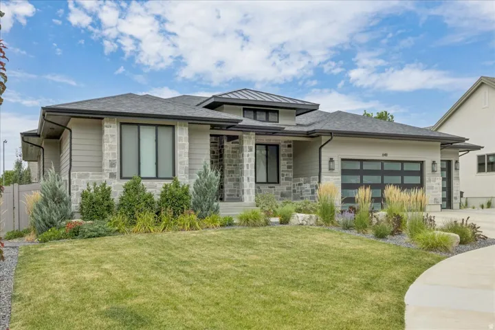 Contemporary exterior featuring stone accents, horizontal siding, dark-framed windows, a modern garage door, and a manicured lawn with varied landscaping