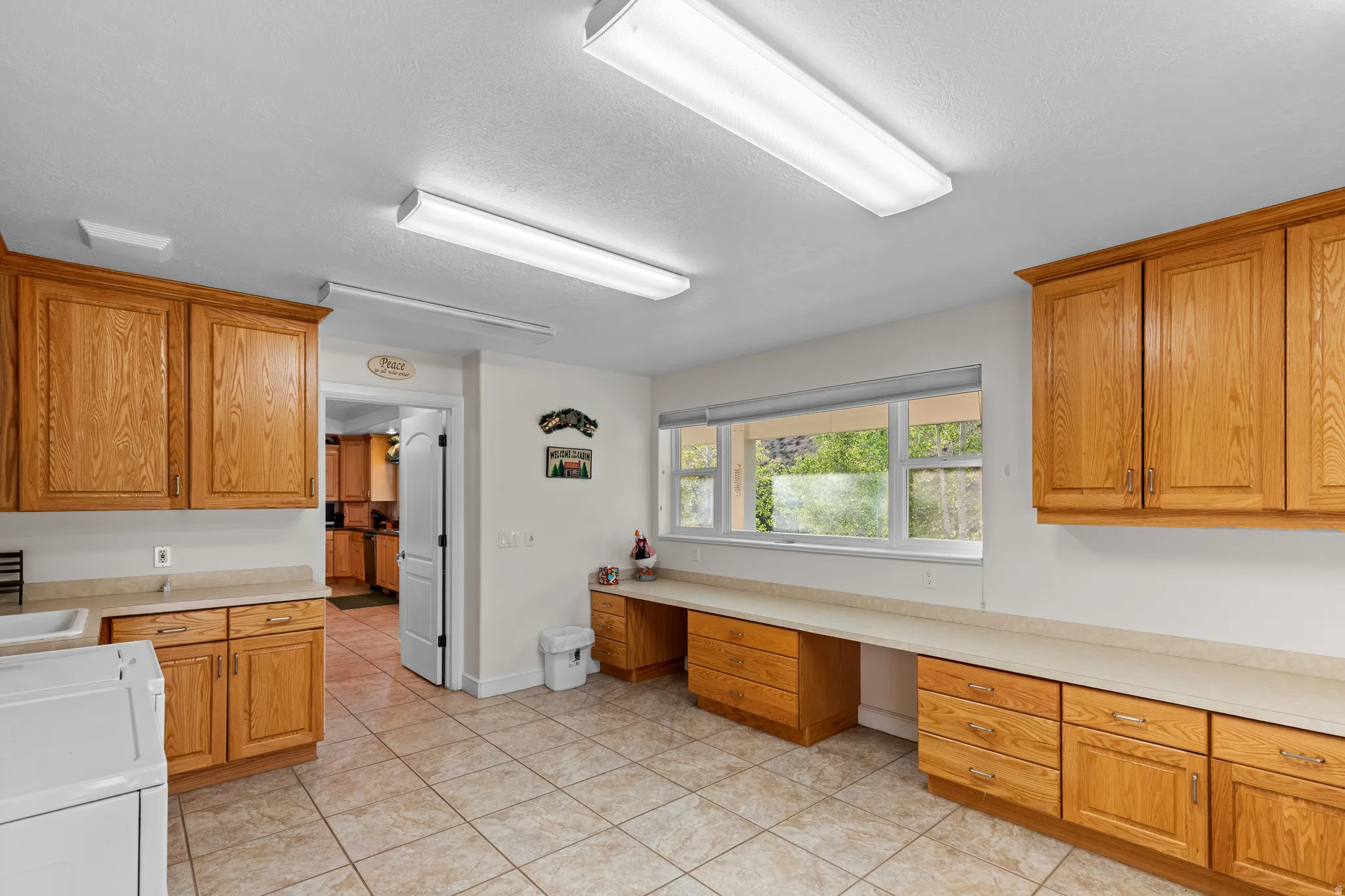 Spacious utility room featuring extensive natural wood cabinetry, light-toned countertops, and a tiled floor