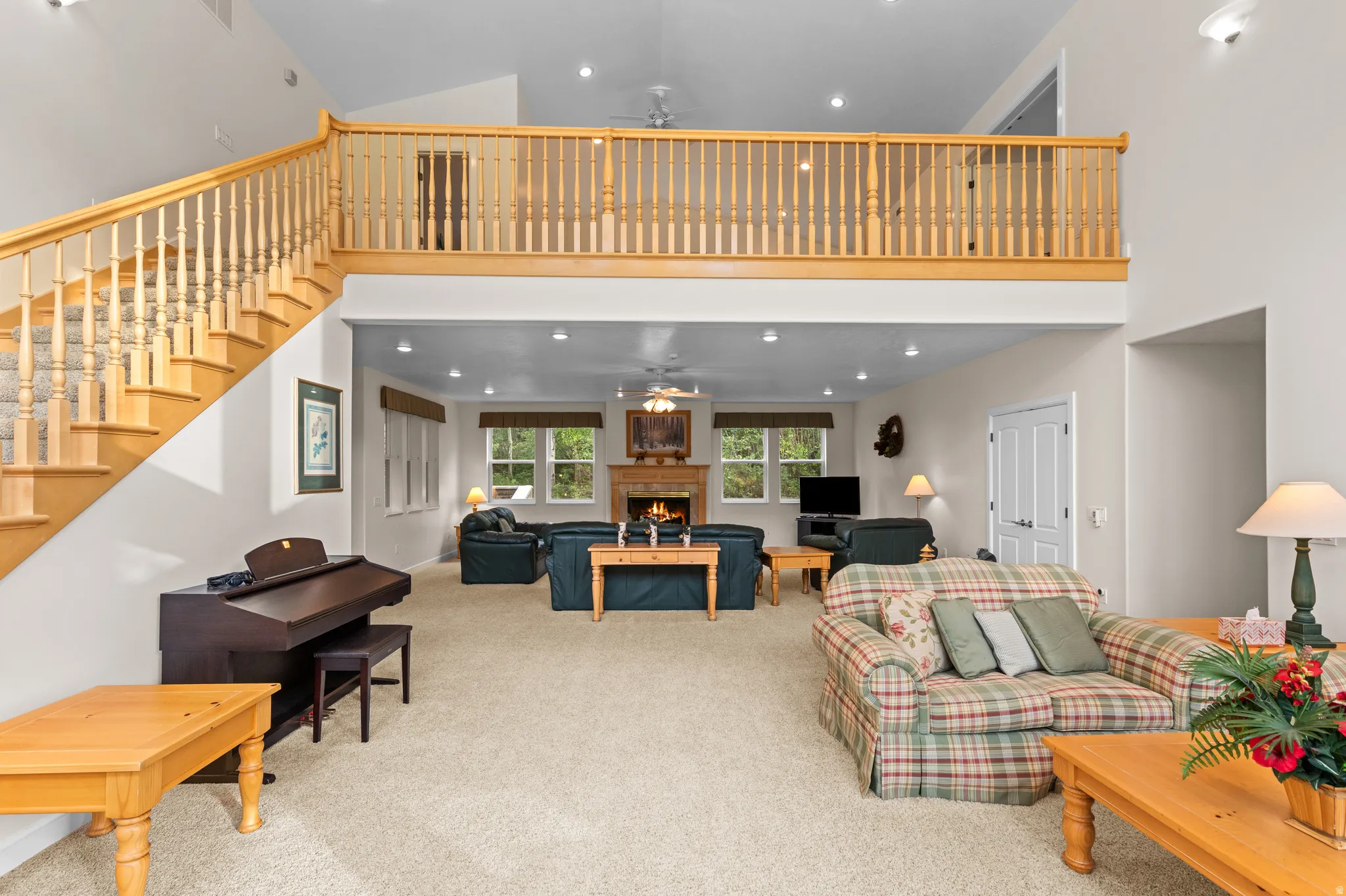 Two-story living area featuring a wood staircase with carpeted treads, a second-story balcony with wood railing, recessed lighting, and a stone-clad fireplace