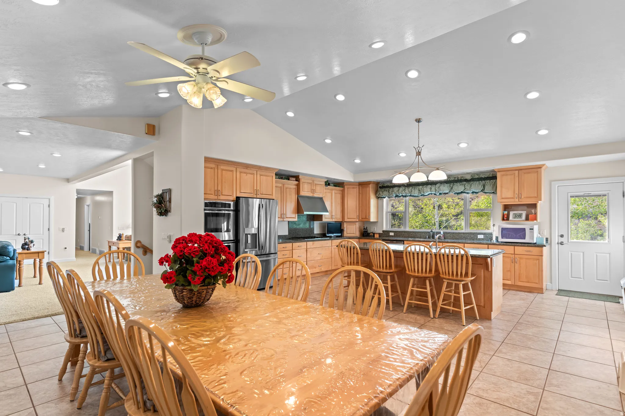 Spacious kitchen and dining area featuring vaulted ceilings, recessed lighting, tile flooring, light wood cabinetry, and a kitchen island with bar seating
