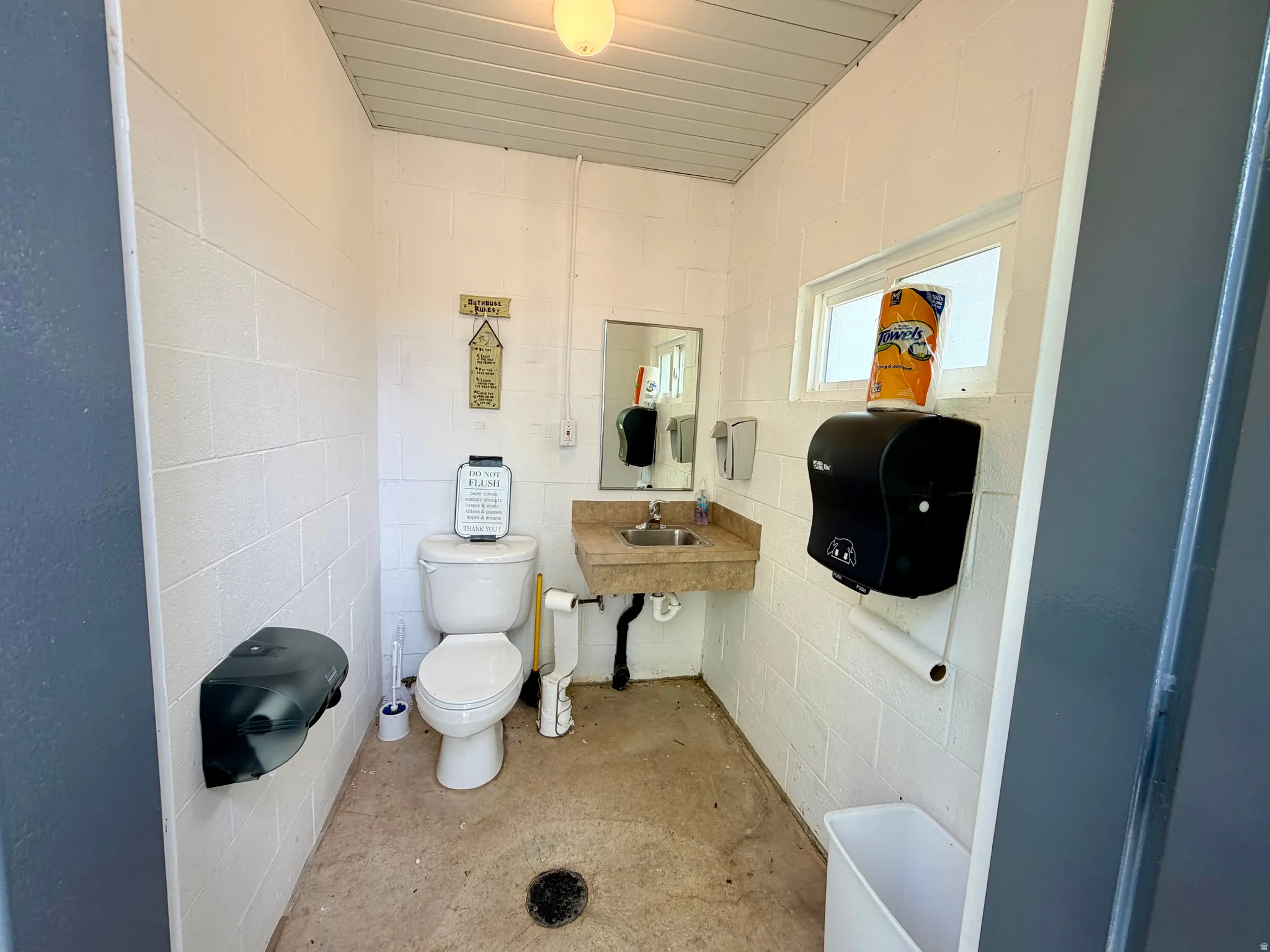 Functional restroom featuring white block walls, a single window, and a ceiling-mounted light fixture