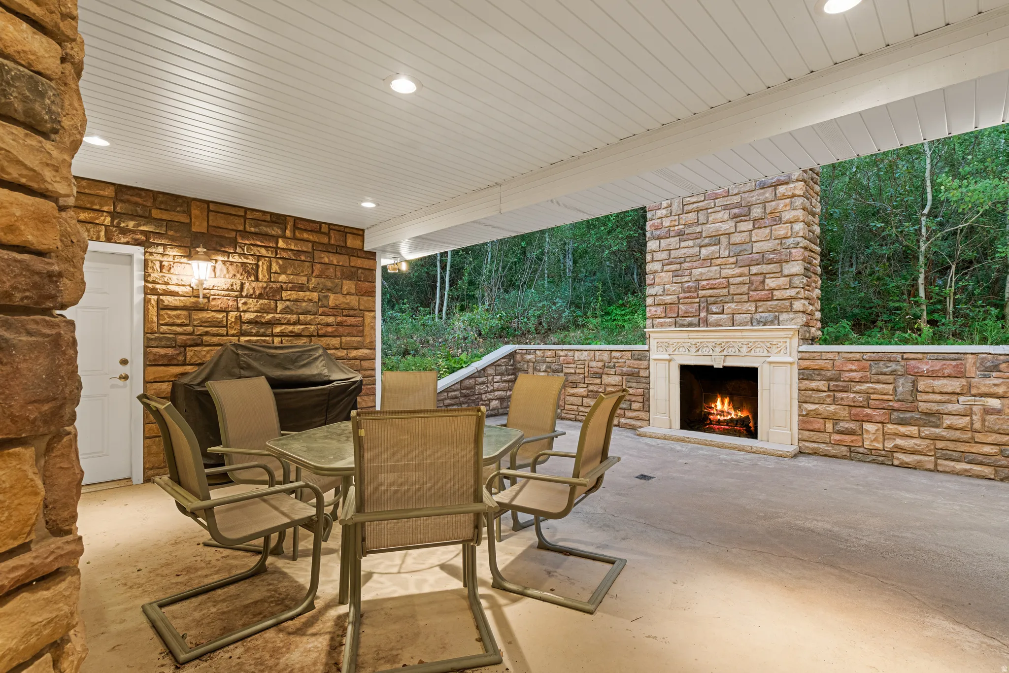 Covered outdoor patio featuring extensive stone wall cladding, a built-in stone fireplace with an ornate mantel, and recessed ceiling lighting