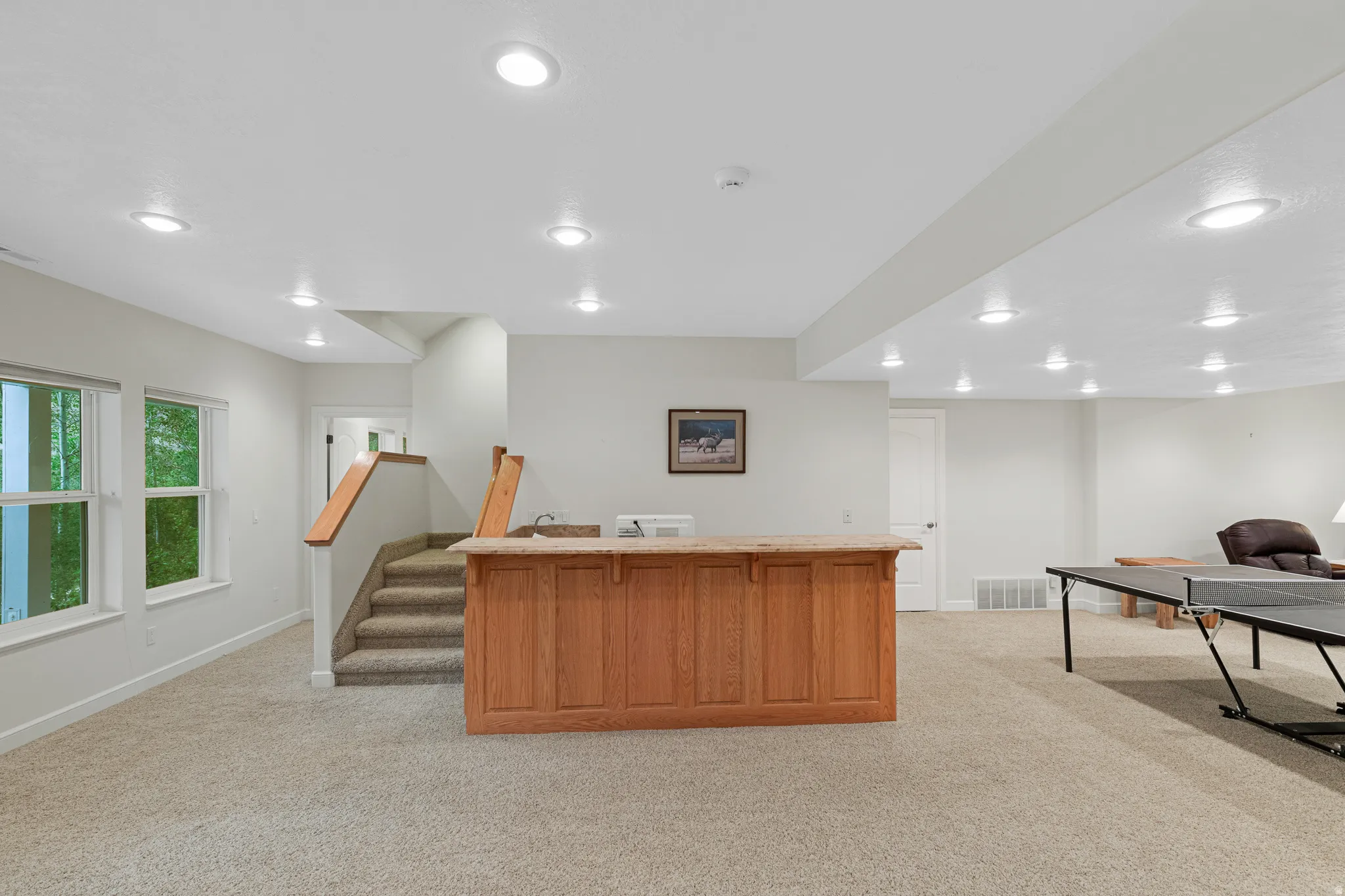 Spacious finished lower level featuring a built-in wood-finish bar with a stone countertop and integrated sink, recessed lighting, carpet flooring, and multiple double-hung windows