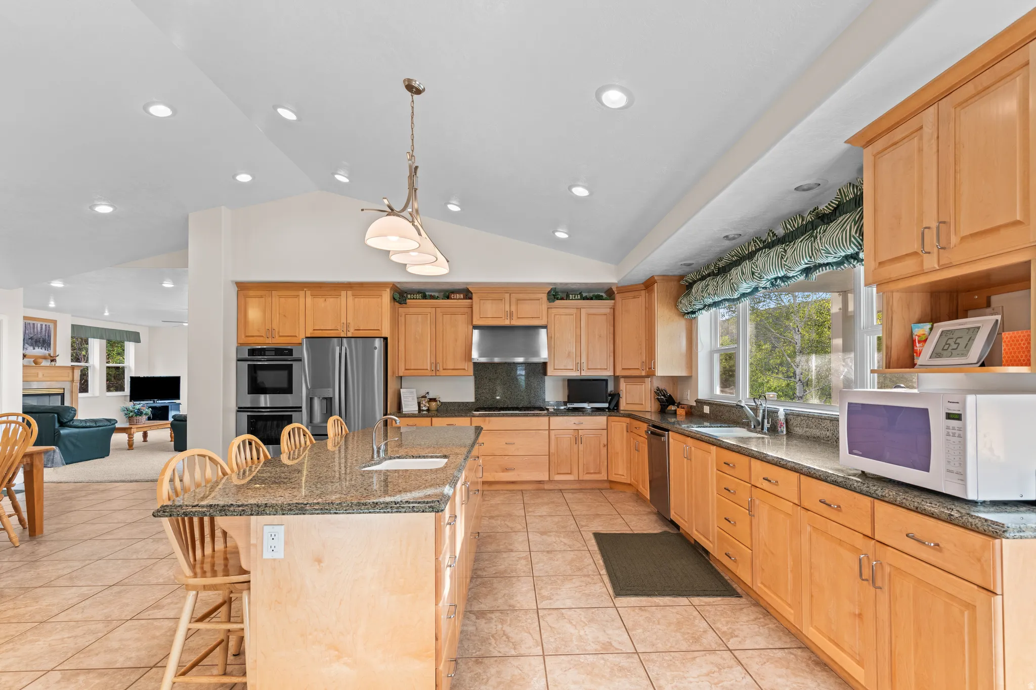 Kitchen featuring light wood cabinetry, granite countertops, tile flooring, stainless steel appliances, and a vaulted ceiling with recessed lighting