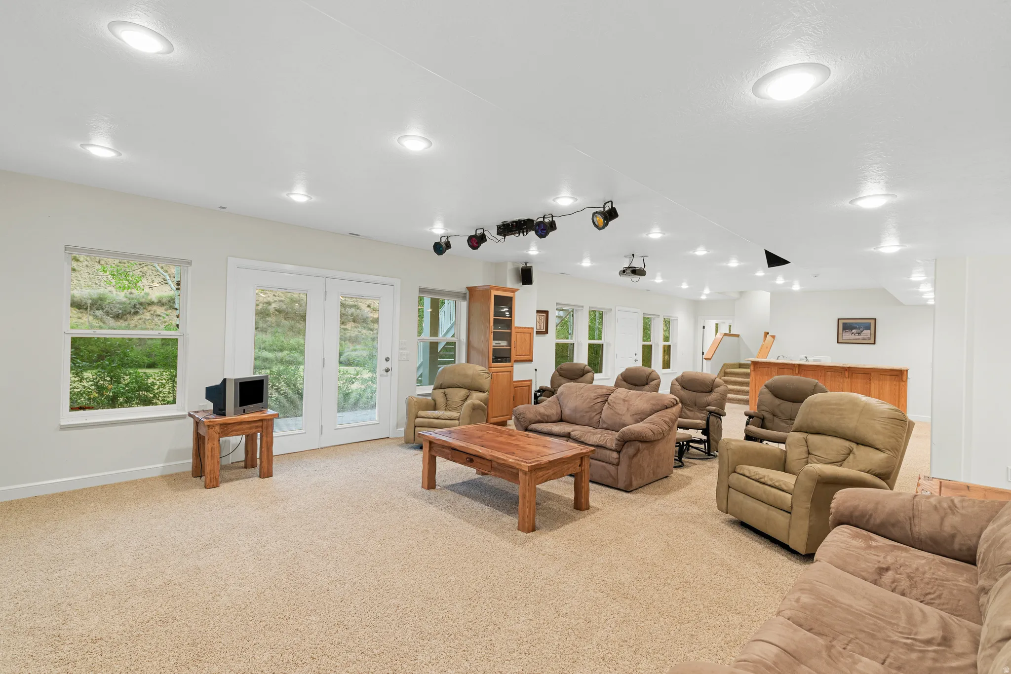 Spacious lower-level room featuring plush carpet flooring, recessed lighting, and multiple windows