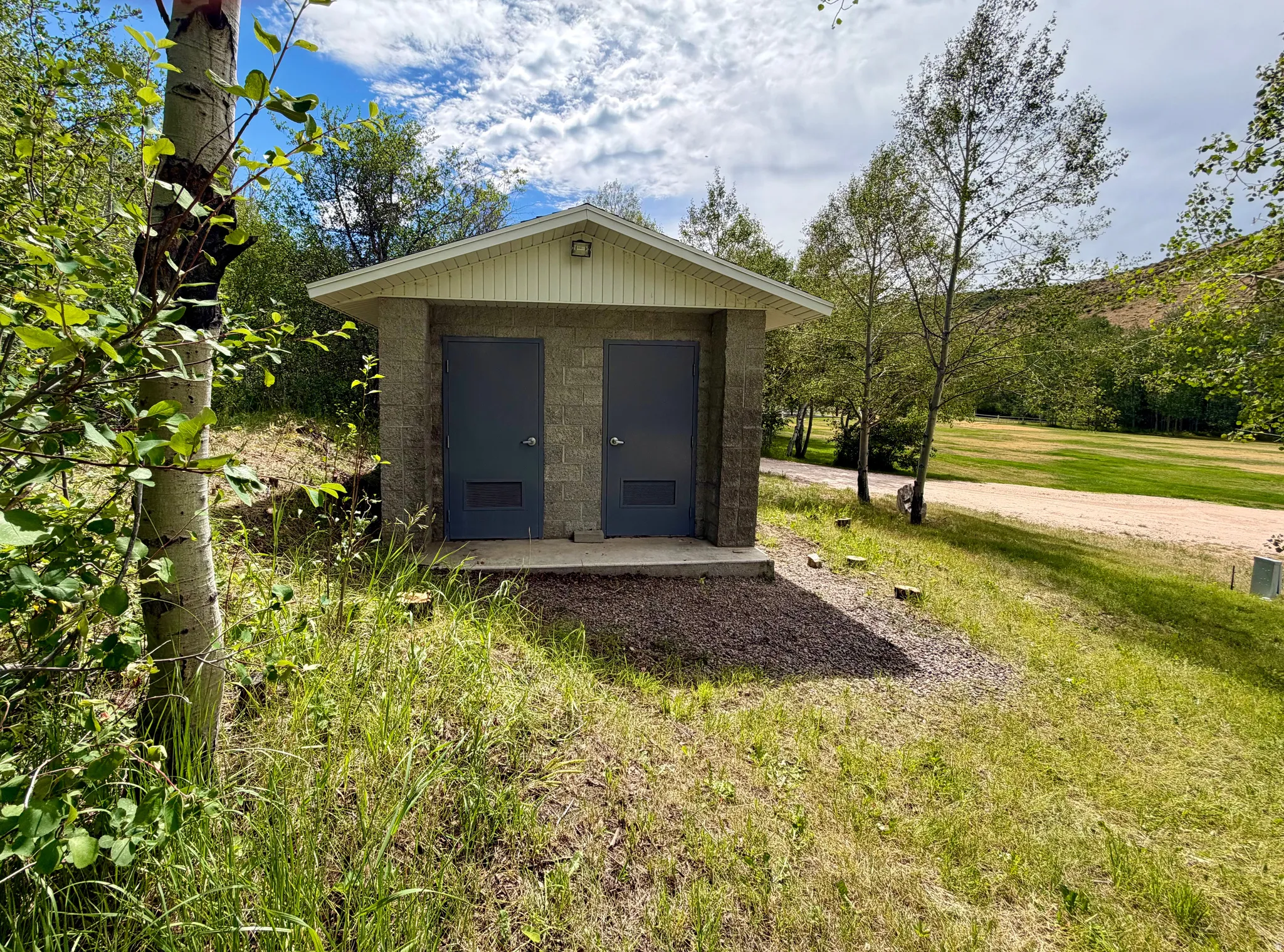 Outside well-built bathroom structure featuring a pitched roof, light-toned siding, and a security light