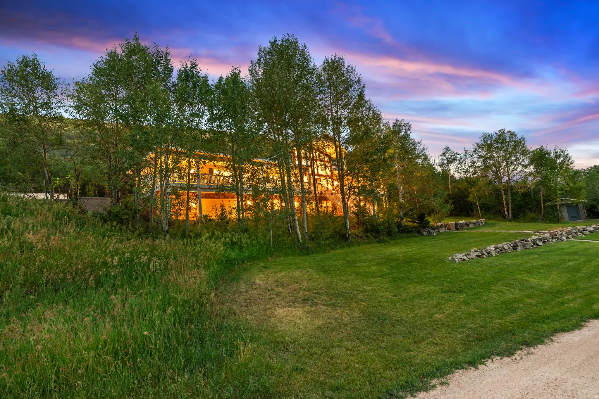 Spacious outdoor area featuring a manicured lawn, natural stone retaining walls, and surrounding mature trees