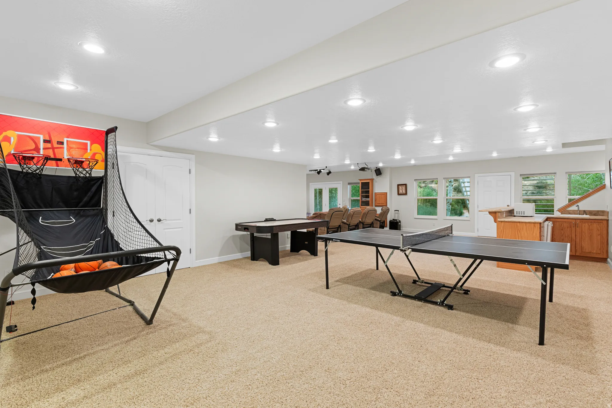 Spacious recreation room featuring recessed lighting, light-toned carpeting, a built-in wet bar with wood cabinetry, and multiple windows