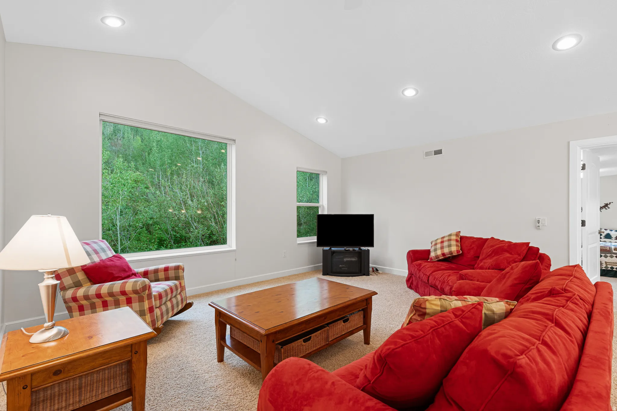 Spacious room featuring vaulted ceilings, recessed lighting, and large windows showcasing abundant natural light and green scenery
