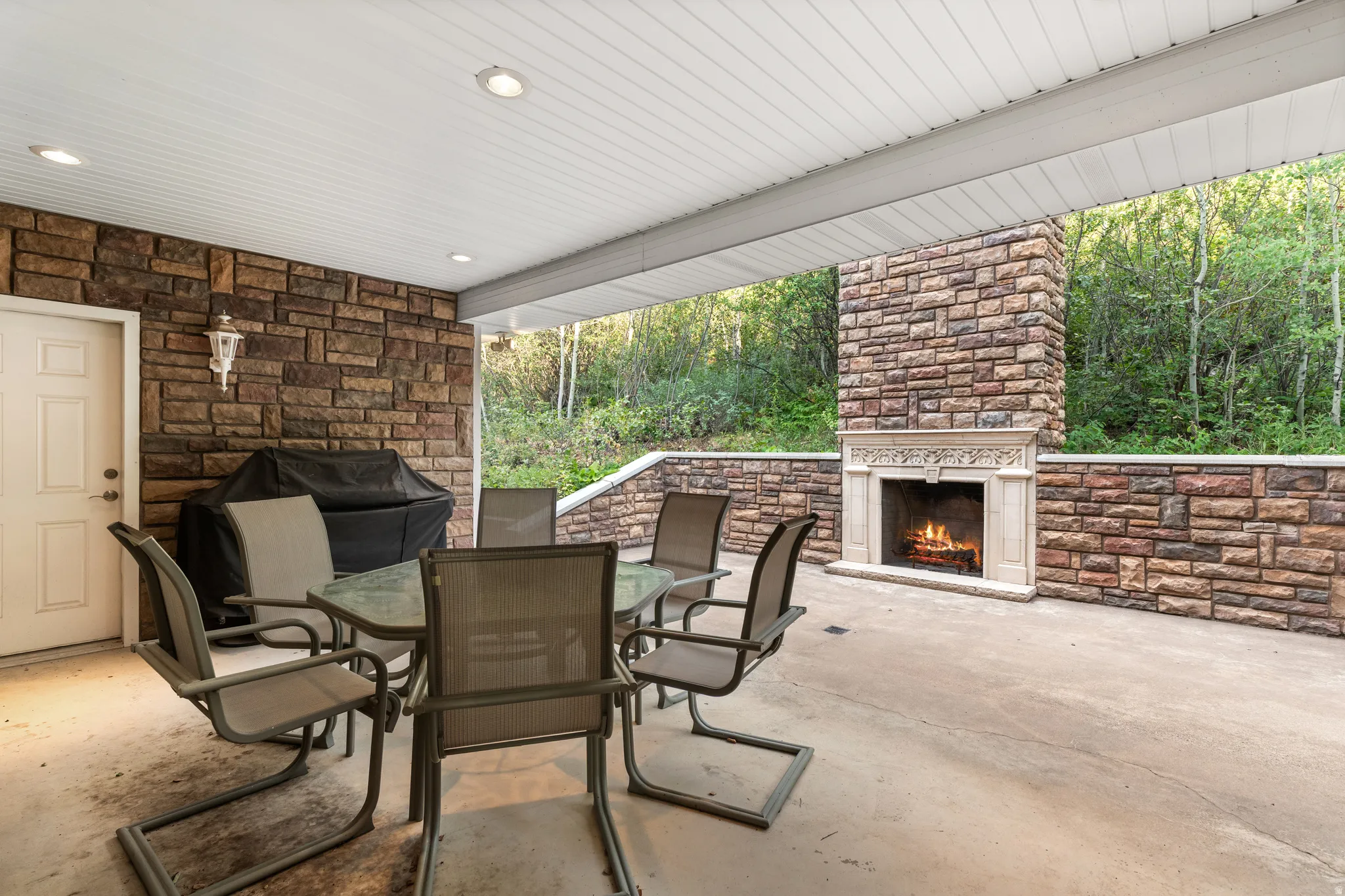Covered outdoor patio featuring stone-clad walls, a built-in outdoor fireplace with an ornate mantel, and recessed ceiling lighting