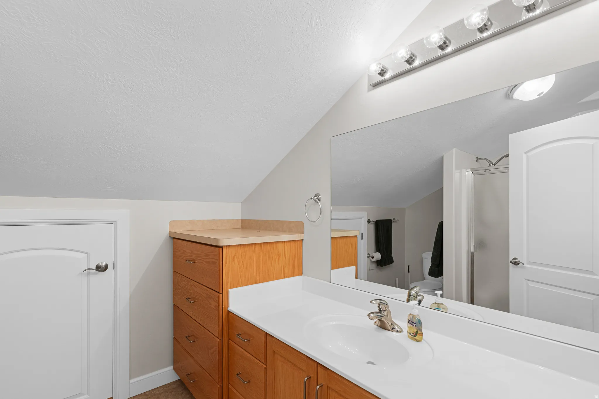 Bathroom vanity featuring a single basin sink and light wood cabinetry, complemented by a large wall-mounted mirror with overhead bar lighting