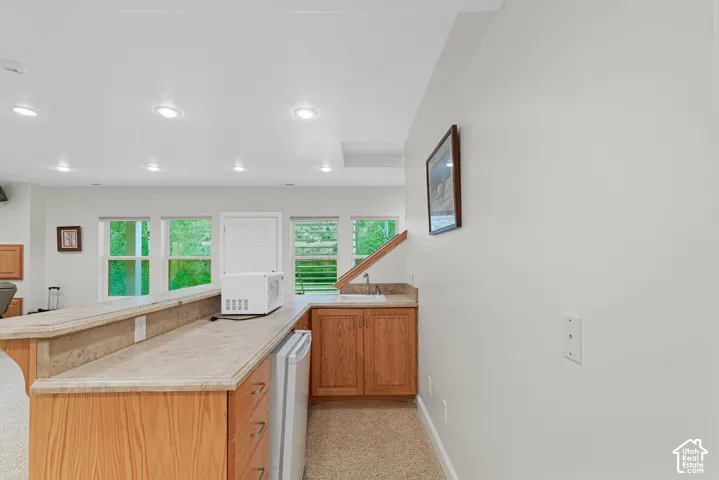 Wet bar featuring wood cabinetry, stone-finish countertops, a built-in sink, and a compact refrigerator