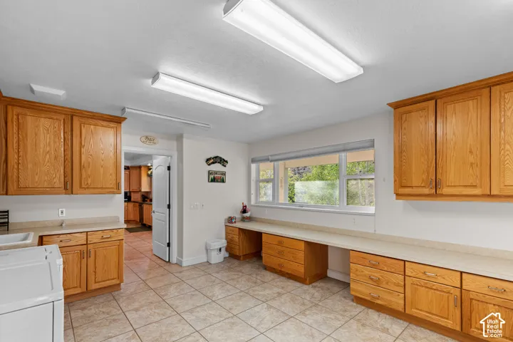 Spacious utility room featuring extensive natural wood cabinetry, light-toned countertops, and a tiled floor