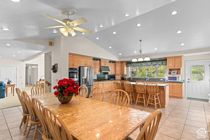 Spacious kitchen and dining area featuring vaulted ceilings, recessed lighting, tile flooring, light wood cabinetry, and a kitchen island with bar seating
