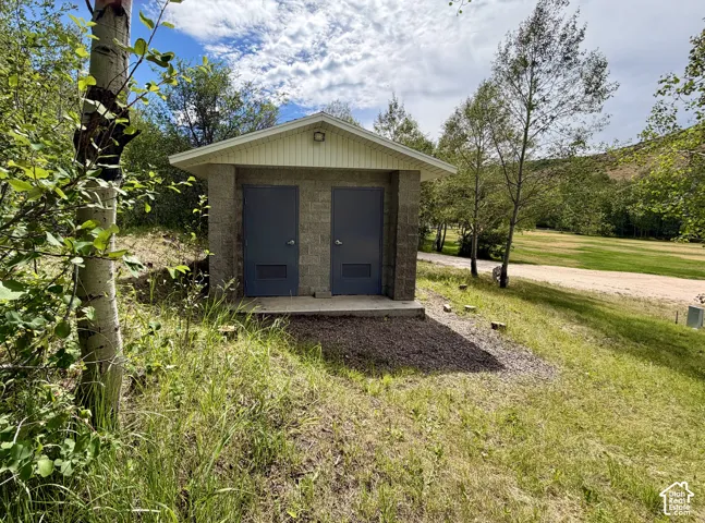 Outside well-built bathroom structure featuring a pitched roof, light-toned siding, and a security light