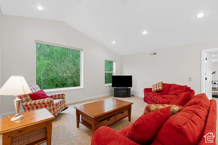 Spacious room featuring vaulted ceilings, recessed lighting, and large windows showcasing abundant natural light and green scenery