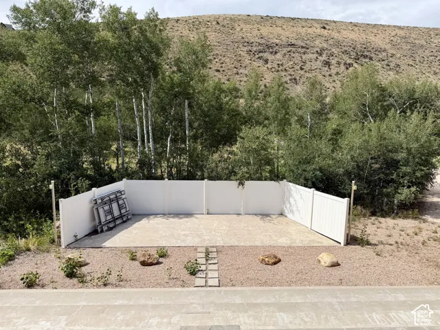 Outdoor paved amphitheater area featuring a white privacy fence, gravel landscaping with decorative rocks, and mature trees in the background