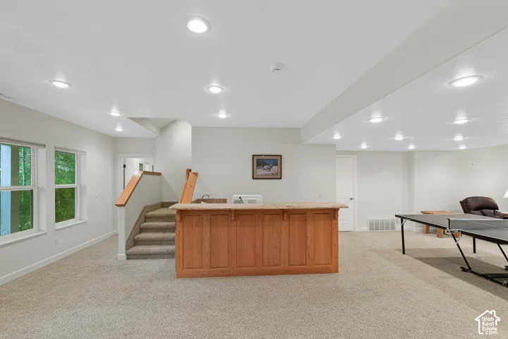 Spacious finished lower level featuring a built-in wood-finish bar with a stone countertop and integrated sink, recessed lighting, carpet flooring, and multiple double-hung windows