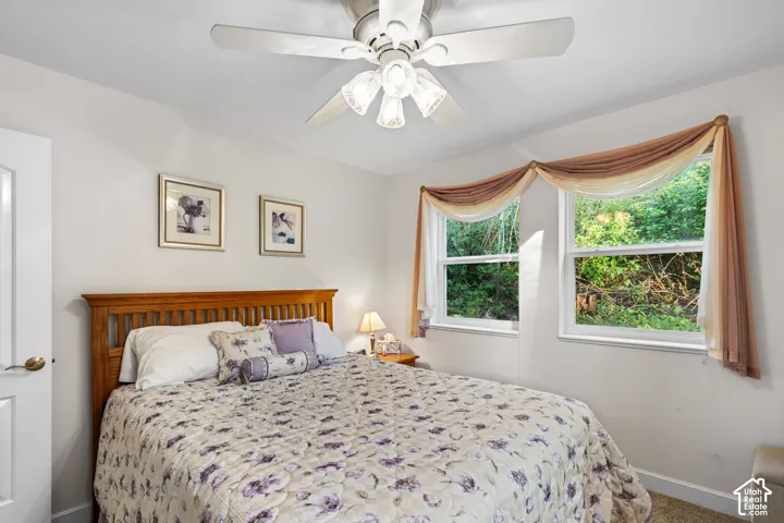 Bedroom featuring twin windows, a ceiling fan with integrated lighting, and light-toned walls