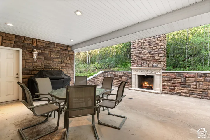 Covered outdoor patio featuring stone-clad walls, a built-in outdoor fireplace with an ornate mantel, and recessed ceiling lighting