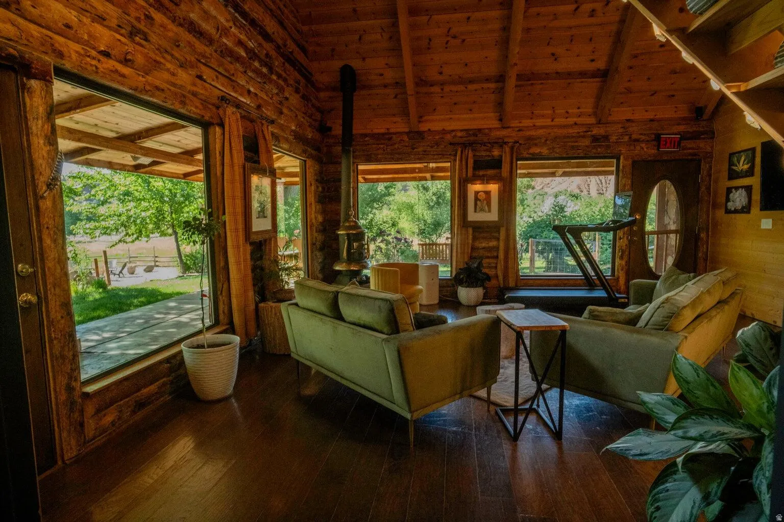 Interior space featuring exposed log walls and ceiling, wood-finish flooring, multiple expansive window placements, and a cylindrical wood-burning stove