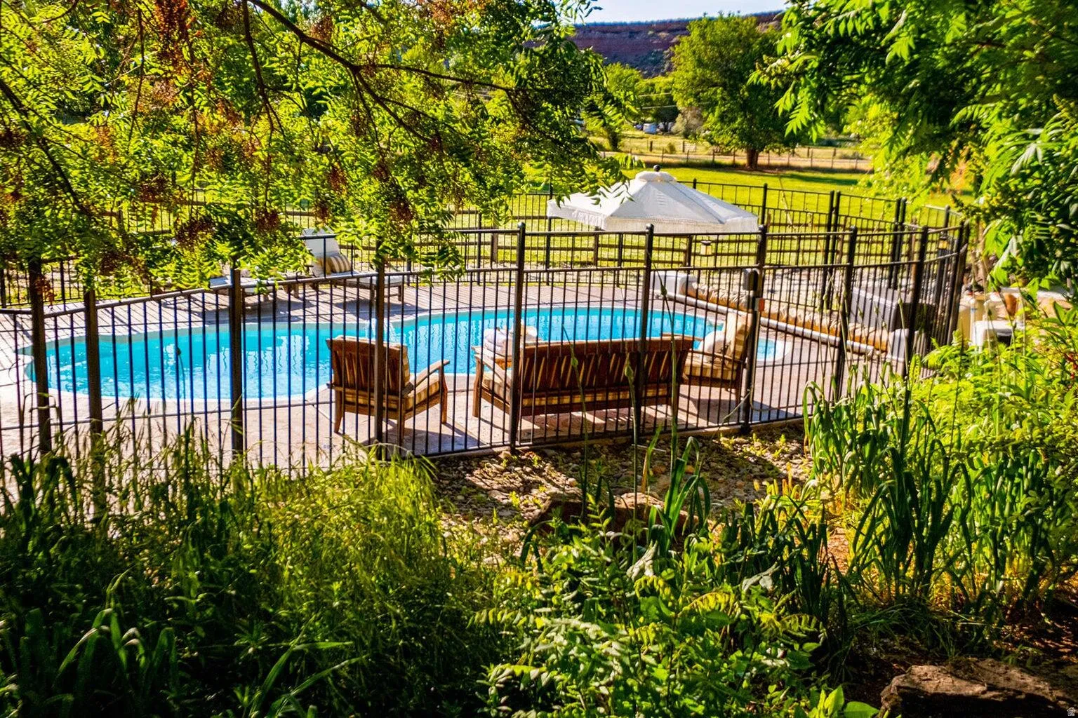 Fenced swimming pool with surrounding patio space and lush perimeter landscaping