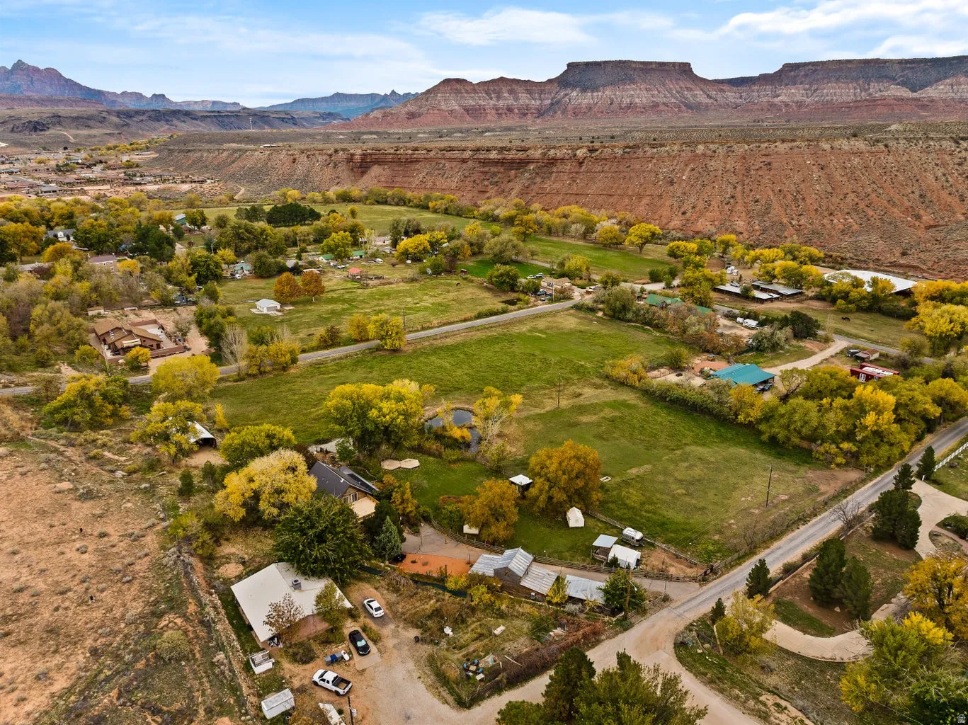 Expansive aerial perspective showcasing a rural landscape with scattered residences, green fields, and mature trees with yellow foliage