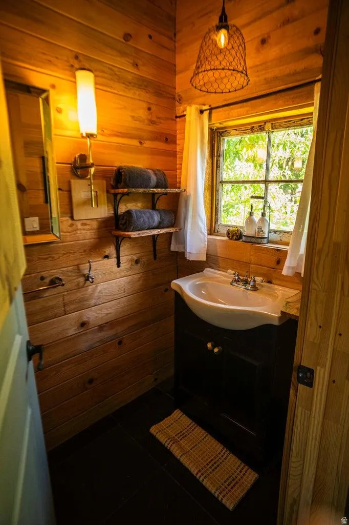 Wood-paneled interior featuring a dark wood vanity with white porcelain sink, wall-mounted sconce lighting, and a window with natural light
