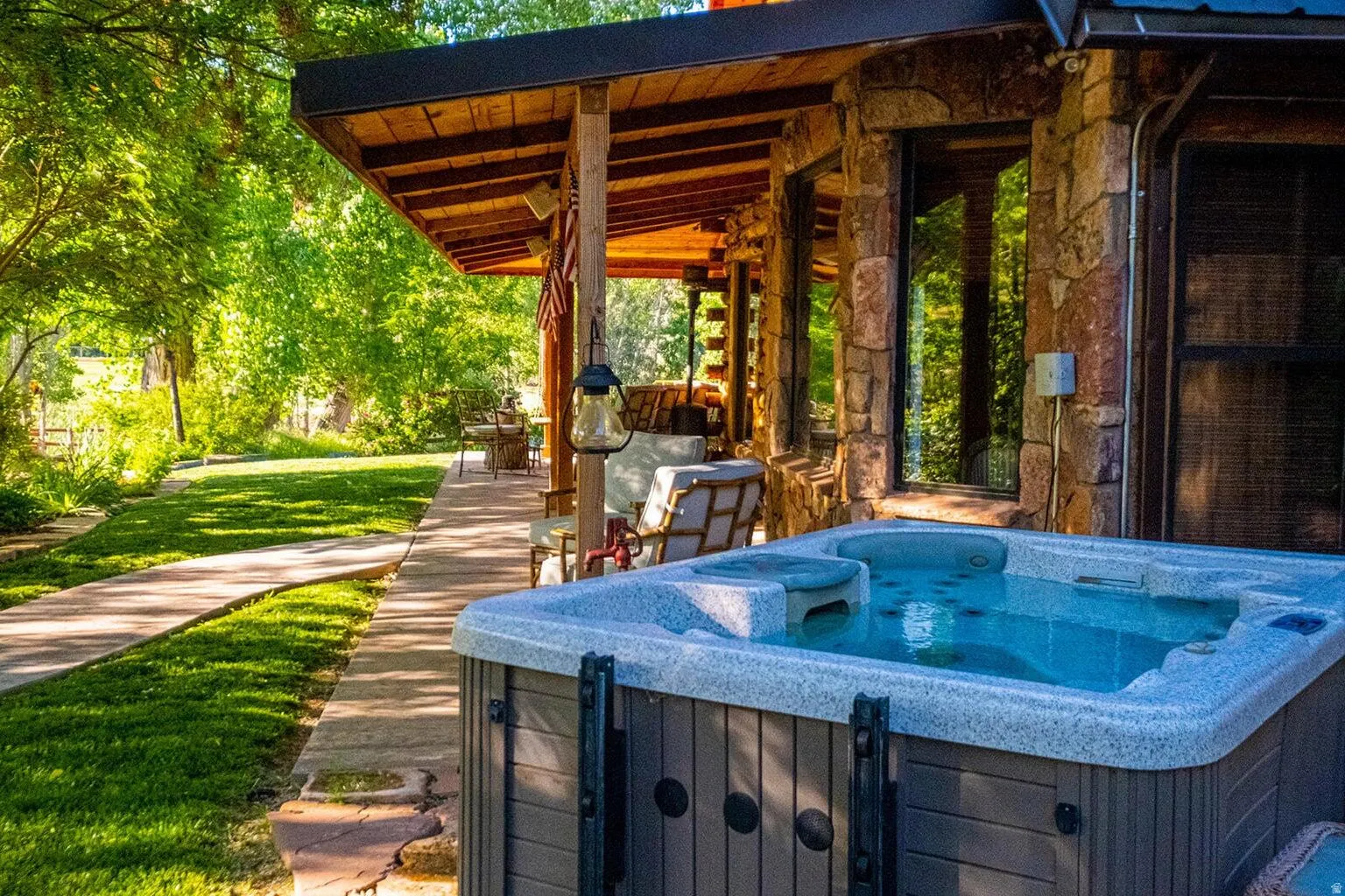 Outdoor spa with stone-clad exterior, covered patio, wood beam ceiling, and verdant landscaping