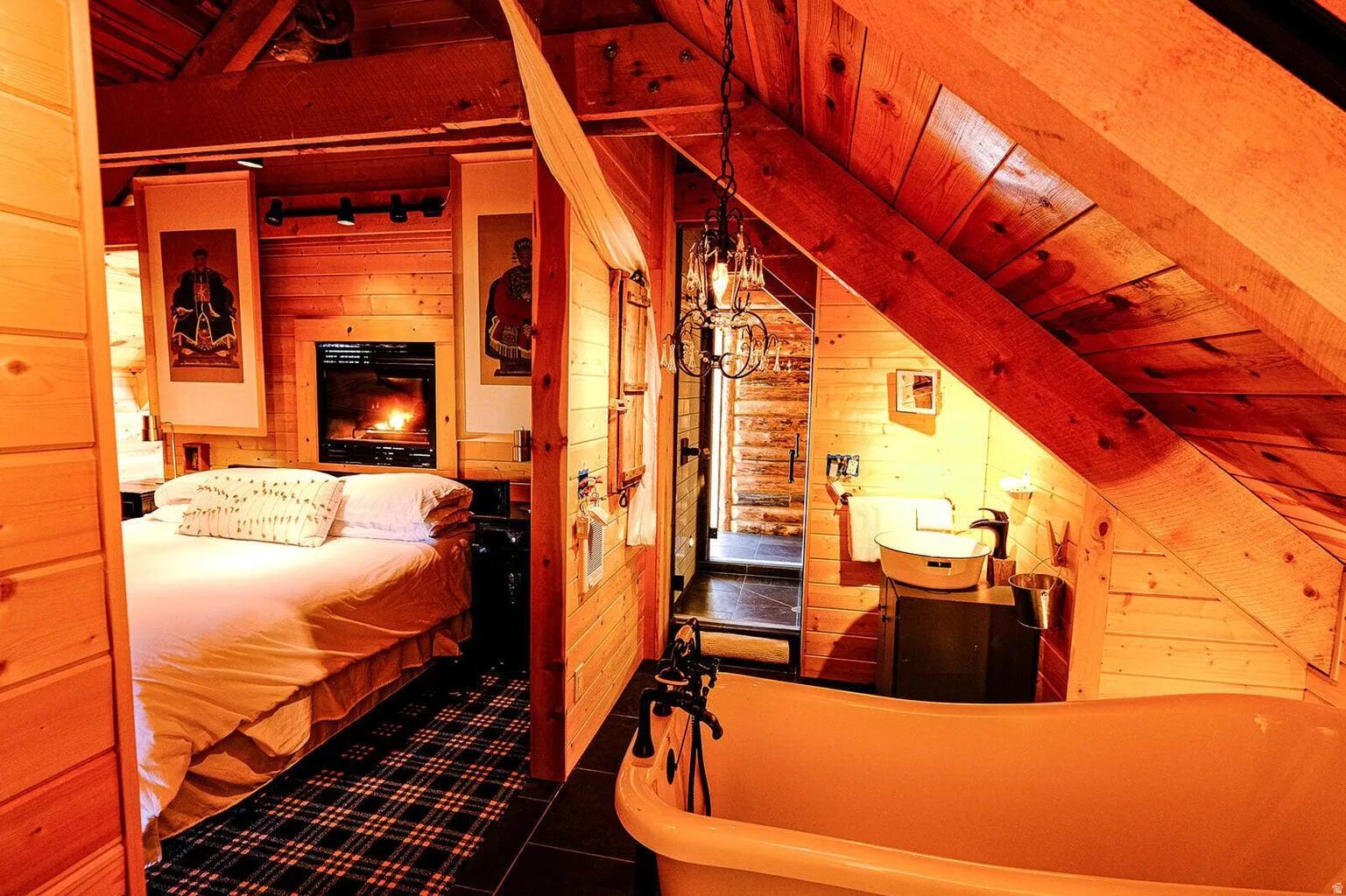 Wood-paneled interior featuring a built-in fireplace, a freestanding clawfoot tub, a vessel sink, an industrial-style chandelier, and dark tile flooring