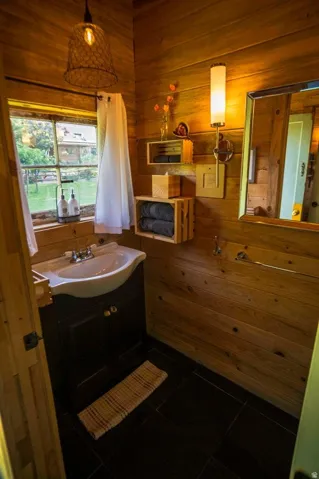 Warm wood-finish paneling throughout this bathroom, featuring a dark vanity with an integrated sink, dark tile flooring, a wall-mounted mirror, and an exposed bulb pendant light