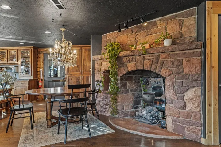 Stone fireplace with hearth, wood-finish flooring, custom wood cabinetry, crystal chandelier, and track lighting