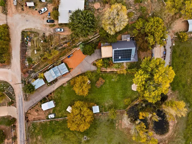 Property featuring a main residence with rooftop solar panels, a substantial green lawn, mature trees, and a visible pond