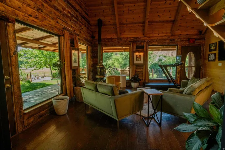 Interior space featuring exposed log walls and ceiling, wood-finish flooring, multiple expansive window placements, and a cylindrical wood-burning stove
