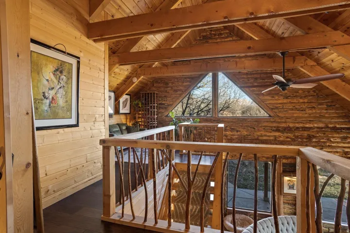 Loft space featuring natural wood plank walls and ceiling, exposed wood beams, wood-finish flooring, and a unique branch-style railing