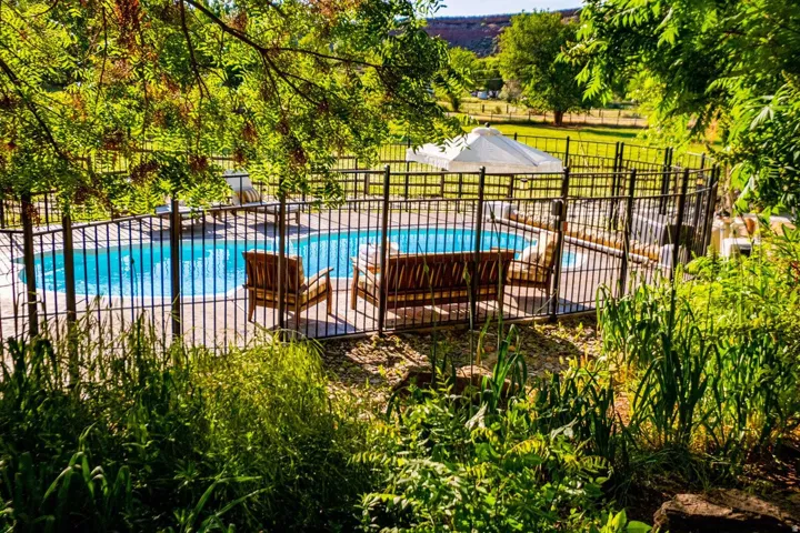 Fenced swimming pool with surrounding patio space and lush perimeter landscaping