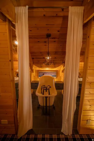 Freestanding clawfoot bathtub set on dark square tile flooring, framed by light-toned wood plank walls and a wood plank ceiling