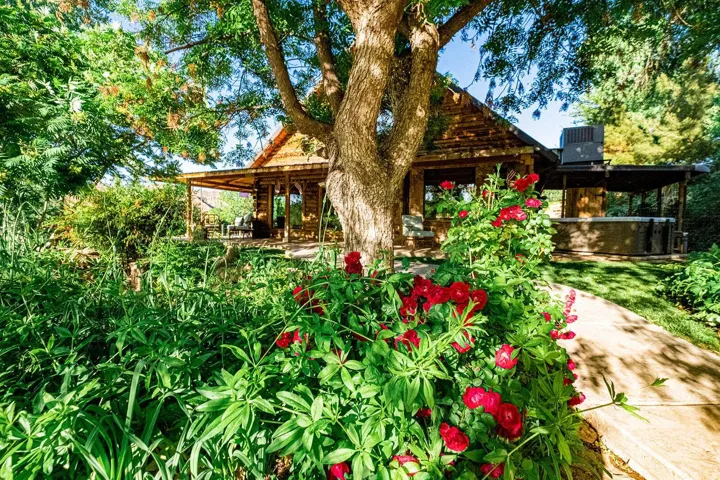 Lush landscaping surrounds a rustic lodge-style structure featuring a covered porch, wood siding, and an exposed aggregate pathway