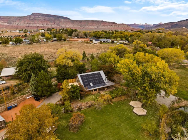 Property featuring a solar-paneled roof, surrounding mature trees, and a manicured lawn