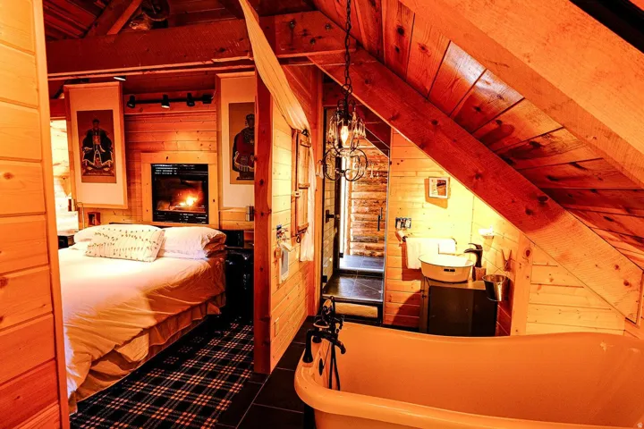 Wood-paneled interior featuring a built-in fireplace, a freestanding clawfoot tub, a vessel sink, an industrial-style chandelier, and dark tile flooring