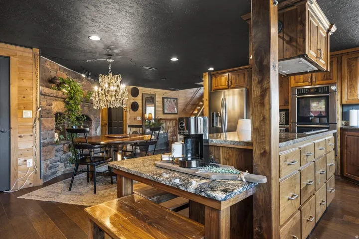 Open-concept kitchen and dining area featuring rich wood cabinetry, stone countertops, stainless steel appliances, and a stone accent wall
